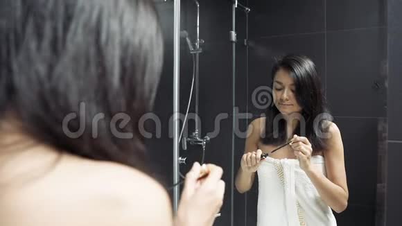 漂亮的年轻女人看着镜子在浴室里给她的眼睛涂上睫毛膏视频的预览图