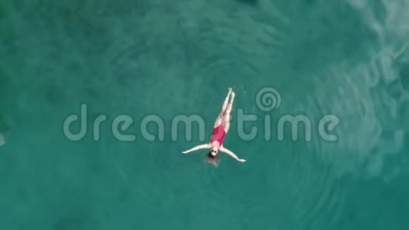 在晶莹剔透的绿松石海洋中年轻漂亮性感的女孩穿着红色泳衣漂浮在水面上快乐视频的预览图