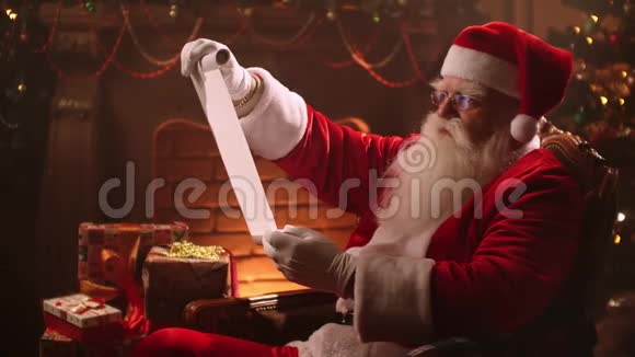 圣诞老人留着胡子穿着西装坐在椅子上读着一本卷轴上面有一张儿童礼物清单视频的预览图