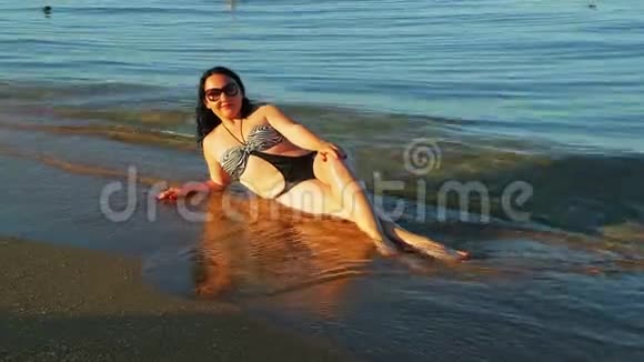 一位深褐色皮肤的女人穿着泳衣在海边水边打日光浴视频的预览图
