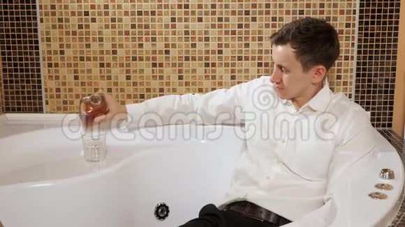 穿着裤子和衬衫的男人躺在浴缸里喝酒视频的预览图