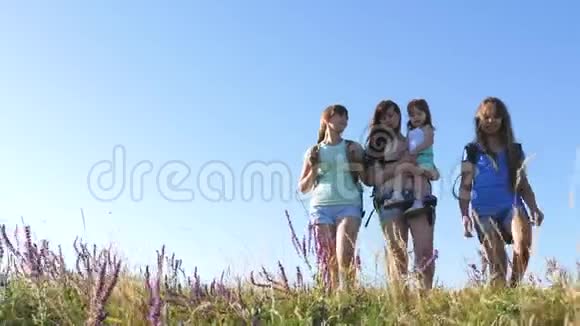 快乐的妈妈和女儿们一个小宝宝在夏天背着彩色的背包穿越田野家庭生活视频的预览图