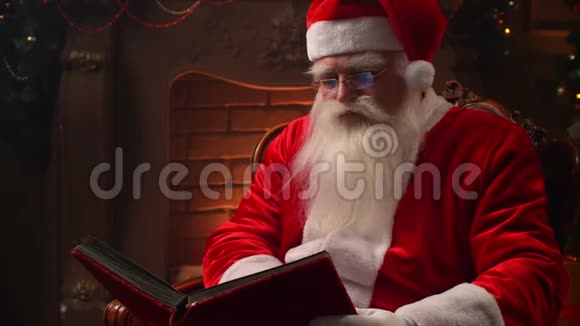 有胡子的老圣诞老人在圣诞树的背景上看书视频的预览图