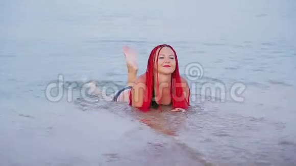 一个穿着红色辫子的黑色泳衣的女人躺在海边的海水里视频的预览图