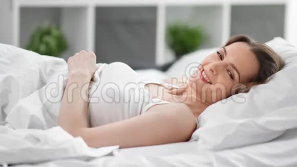 迷人的年轻女性躺在舒适的床上享受早晨4k龙红色摄像机视频的预览图