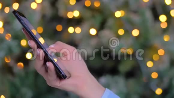 女士手使用智能手机圣诞灯背景侧面近景视频的预览图