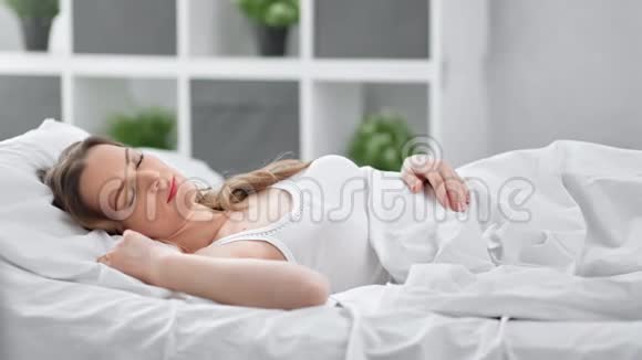 性感的女人在舒适的白色卧室里摆姿势醒来4k龙红相机视频的预览图