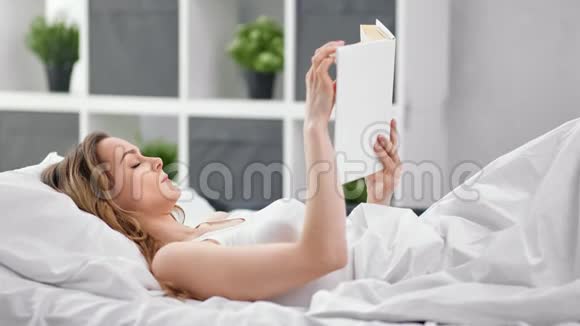 放松的年轻女性躺在舒适的床上看书4k龙红相机视频的预览图