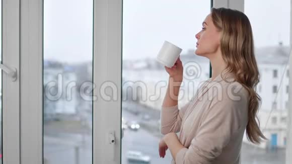 漂亮的金发美女喝着茶望着窗户4K红色相机拍摄视频的预览图