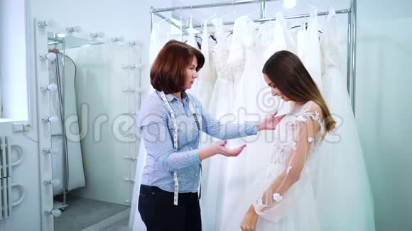 女裁缝在美容院检查年轻新娘的婚纱视频的预览图