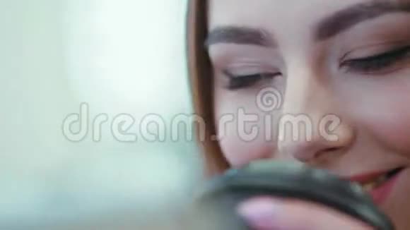一个棕色眼睛的黑发女孩幸福地朝平板电脑屏幕微笑喝着咖啡近距离观看视频的预览图