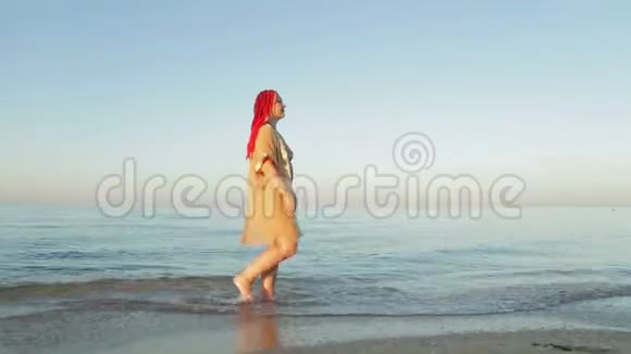 一个穿着泳衣和黄色浴袍的女人在海边散步视频的预览图