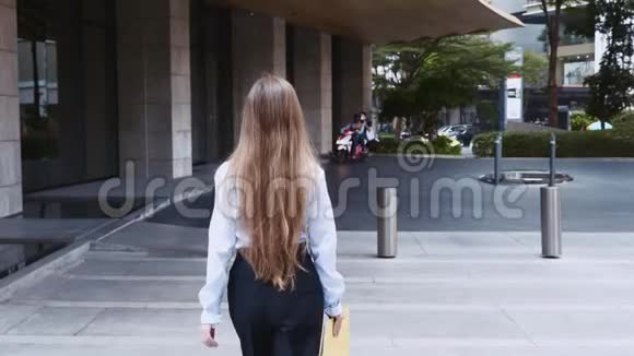 青年商务女性手拿文件夹走在办公楼旁视频的预览图