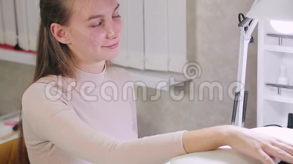 美容院的女美甲师给顾客的指甲涂上紫色的凝胶油那女孩用干指甲的方法视频的预览图