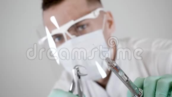 戴面具的牙医专家手拿牙科工具和注射器的肖像视频的预览图