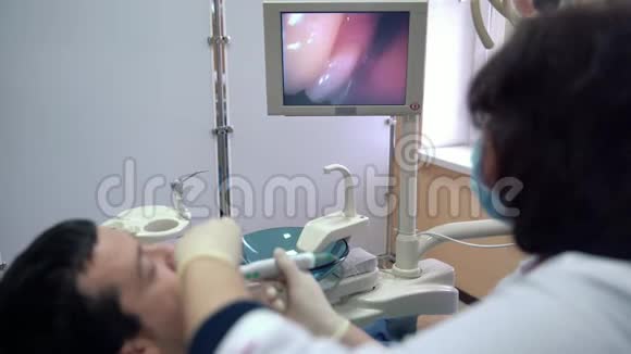 女牙医用口腔内照相机检查病人的牙齿并在监视器上显示结果视频的预览图