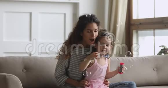 可爱的小女孩和妈妈在家吹肥皂泡视频的预览图