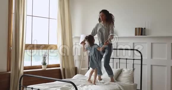 年轻有爱的母亲和幸福的孩子女儿跳在床上视频的预览图