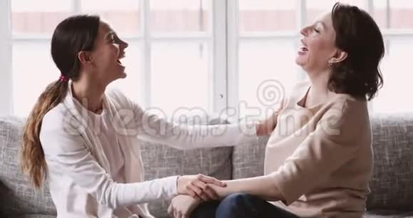 快乐成熟的妈妈和小女儿在沙发上笑着拥抱视频的预览图