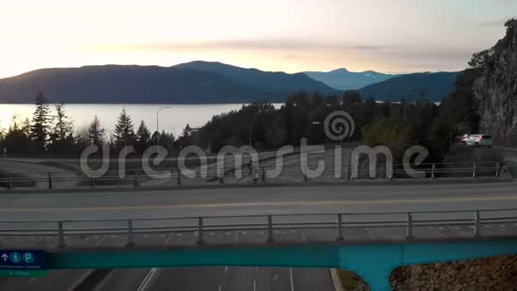 一名男子站在公路上的桥上用数码单反相机在三脚架上拍摄照片俯瞰美丽的海洋视频的预览图