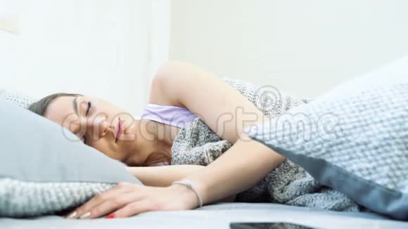 熟睡的年轻女子关掉手机上的闹钟把它藏在枕头下继续睡觉视频的预览图