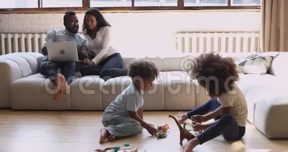 非裔美国人夫妇在孩子们在地板上玩耍时使用笔记本电脑视频的预览图