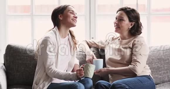 成熟的母亲和小女儿在沙发上聊着喝茶视频的预览图