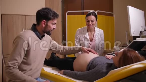 幸福的男人在诊所抚摸怀孕妻子的腹部视频的预览图