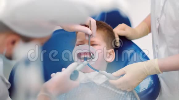男孩坐在由医务人员包围的口腔科扶手椅上中型近距离拍摄4k红色相机视频的预览图