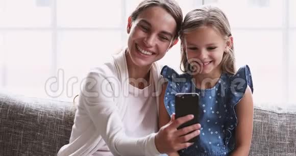 可爱的妈妈在智能手机上播放可爱的小女儿搞笑视频视频的预览图