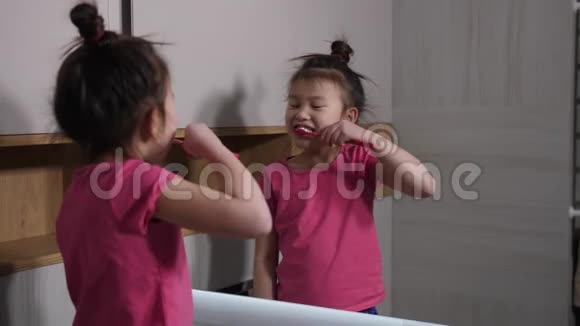 可爱的亚洲女孩在浴室的镜子里刷牙视频的预览图