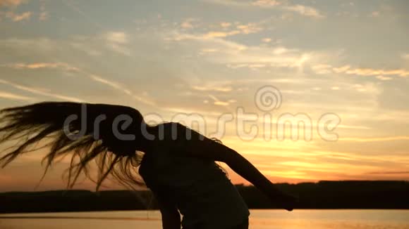 女孩在日落时跳舞长发在夕阳的光线下女人在海滩派对上跳舞时点亮了灯晚上晚上视频的预览图
