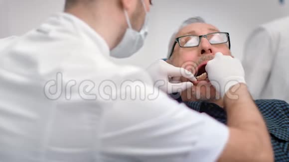 关闭男性牙医尝试假颌样本给资深男子在牙科4k龙红相机视频的预览图