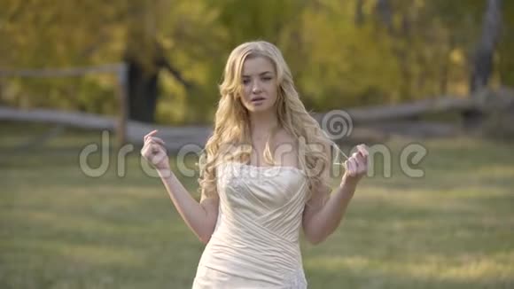 美丽的金发新娘在秋天公园的阳光下摆姿势视频的预览图