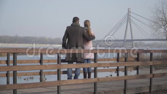 在城市公园的河岸上一对快乐的白人夫妇在聊天和拥抱对爱的男人和女人的看法视频的预览图