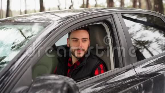 年轻迷人的白人男子坐在他的汽车车轮阳光明媚的冬天视频的预览图