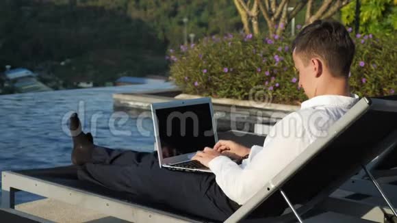 商人用笔记本电脑对付森林和酒店游泳池视频的预览图