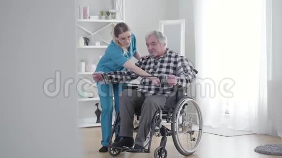 长镜头集中白人妇女帮助老人伸展弹性带与退休人士一起参加视频的预览图