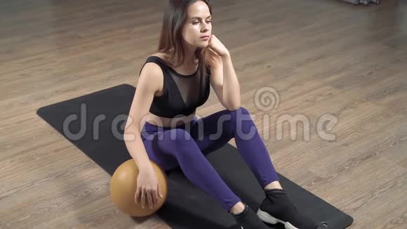 年轻女子手拿健身球在工作室或家里的地板上锻炼后休息视频的预览图