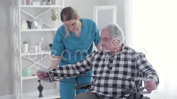 职业护士穿着蓝色制服和眼镜帮助老年残疾人在养老院锻炼无效投标视频的预览图
