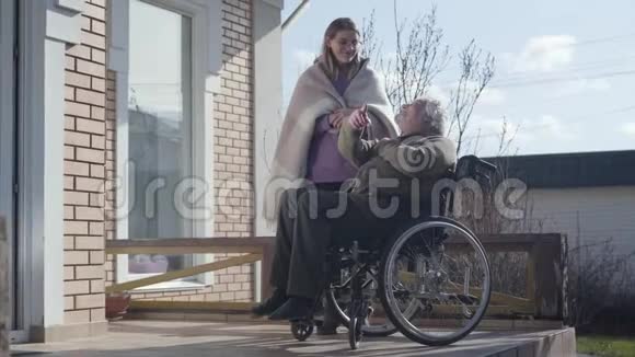 戴眼镜的成年白种人护士和坐在轮椅上的残疾老人交谈微笑着无效投标支出视频的预览图
