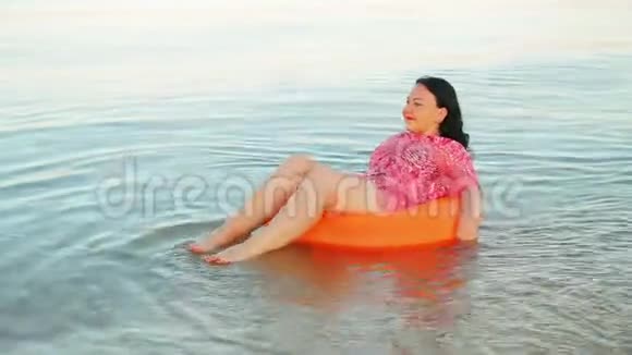 一个黑发女人在海边的游泳圈里微笑视频的预览图