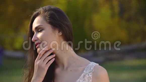 秋天公园里一位留着长发深褐色头发的美丽女人在阳光下摆姿势视频的预览图