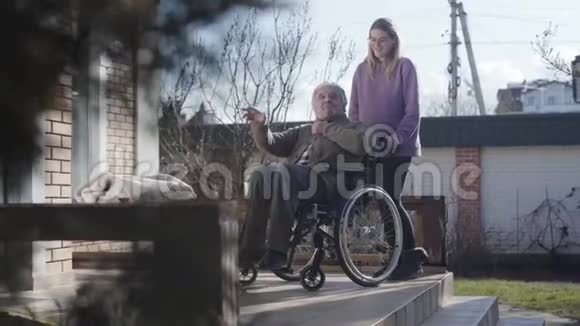 长镜头的成年女性无效的温柔与老白种人交谈和滚动轮椅离开微笑护士视频的预览图