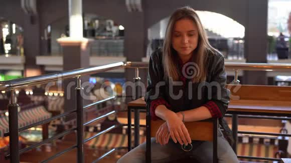 一个漂亮的现代年轻的欧洲女孩穿着黑色皮夹克和牛仔裤留着白发坐在秋天的室内咖啡馆里视频的预览图