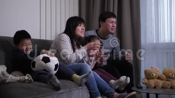 亚洲家庭在家庭房间里看足球比赛视频的预览图
