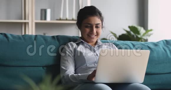 印度女人用笔记本电脑坐在家里的沙发上视频的预览图