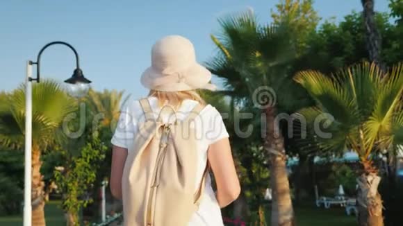 一个背着粉色背包的游客沿着棕榈树大道散步休息和新印象视频的预览图