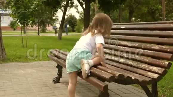 快乐的小女孩爬上一个大公园长凳快乐的小孩站在公园的长凳上幸福童年的概念视频的预览图