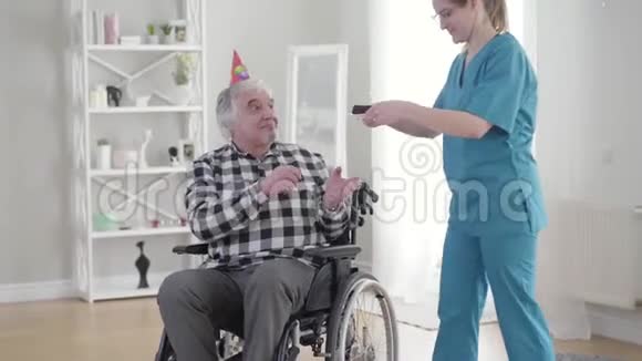 白种人穿着蓝色制服戴着眼镜给残疾人送生日蛋糕快乐的退休老人视频的预览图